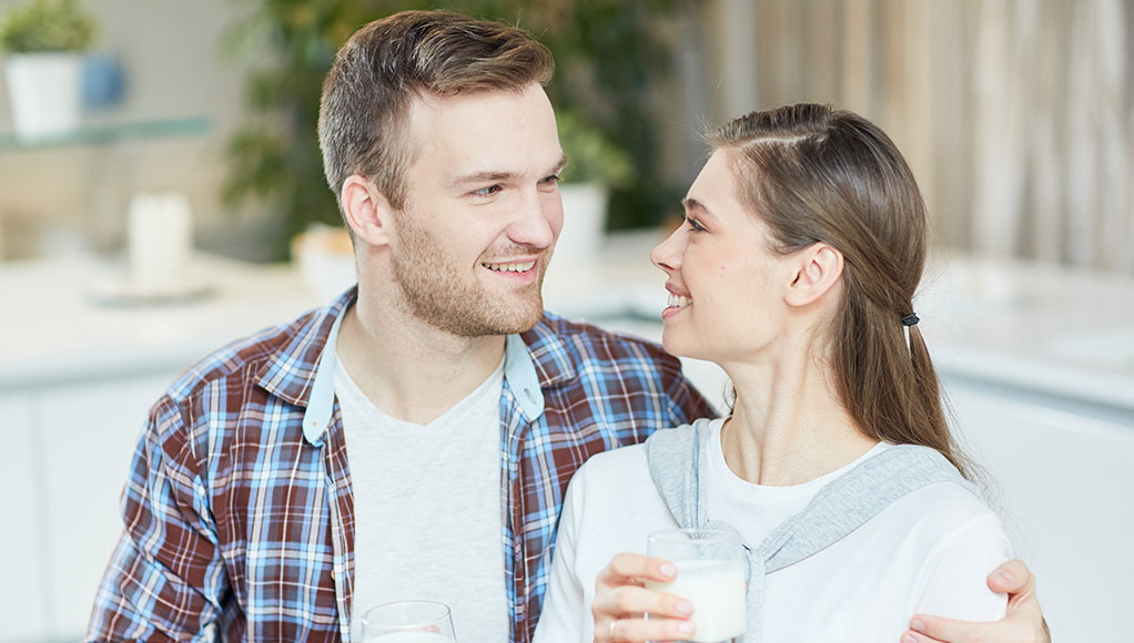 A young couple looking at each other drinking a glass of milk each